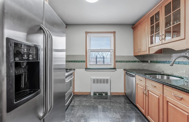 kitchen with decorative backsplash, appliances with stainless steel finishes, dark stone counters, sink, and radiator heating unit