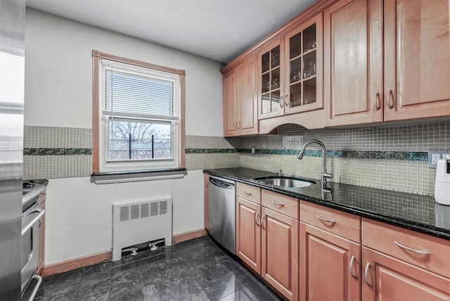 kitchen with backsplash, radiator, stainless steel appliances, sink, and dark stone countertops