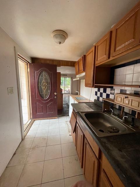817 Southard St, Baldwin, NY 11510 - kitchen with dark countertops, brown cabinets, decorative backsplash, a sink, and under cabinet range hood