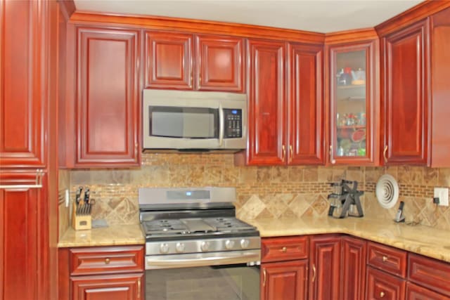 kitchen with backsplash, light stone counters, and stainless steel appliances