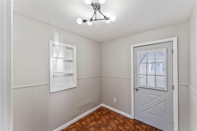 doorway featuring dark parquet floors, wood walls, and an inviting chandelier