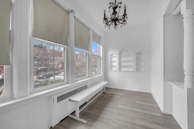 hall featuring decorative columns, light wood-type flooring, radiator heating unit, and a chandelier