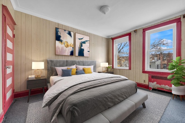 carpeted bedroom featuring wood walls, ornamental molding, and radiator