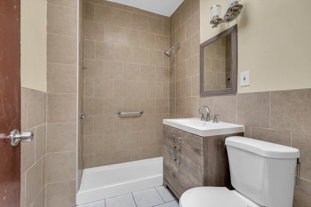 bathroom with vanity, tile patterned flooring, toilet, tiled shower, and tile walls