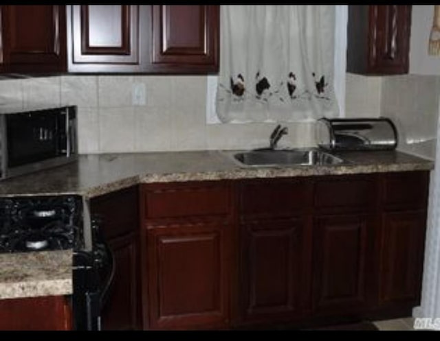 kitchen featuring black gas range, backsplash, light stone counters, and sink