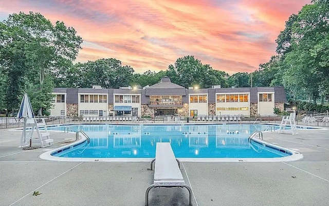 pool at dusk featuring a patio area and a diving board