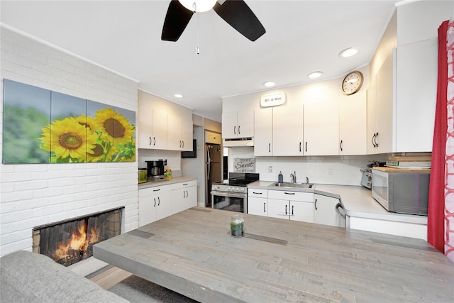 kitchen featuring appliances with stainless steel finishes, light wood-type flooring, a fireplace, sink, and white cabinets