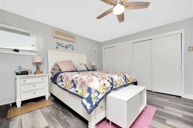 bedroom with a wall mounted AC, ceiling fan, hardwood / wood-style floors, and multiple closets