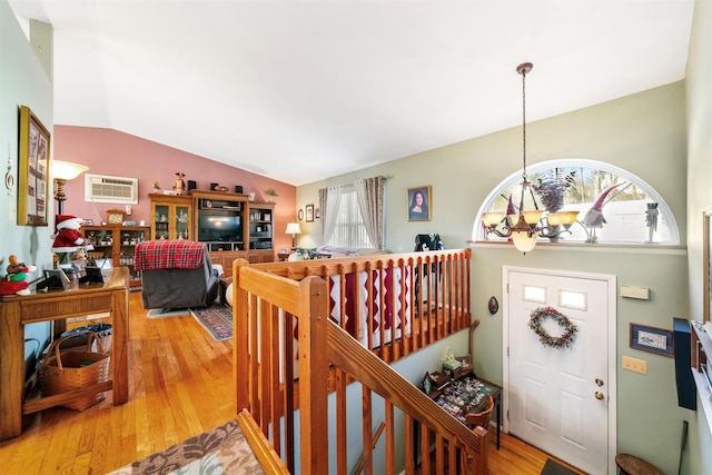 foyer with a chandelier, wood-type flooring, a wall mounted air conditioner, and lofted ceiling