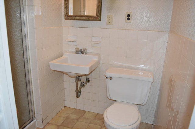 bathroom with sink, a shower with door, tile walls, and toilet