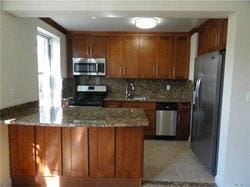 kitchen with light stone countertops, sink, stainless steel appliances, tasteful backsplash, and kitchen peninsula