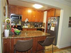 kitchen featuring a kitchen bar, kitchen peninsula, stainless steel appliances, and stone counters