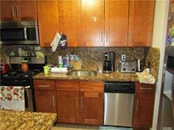 kitchen with decorative backsplash, light stone countertops, sink, and appliances with stainless steel finishes