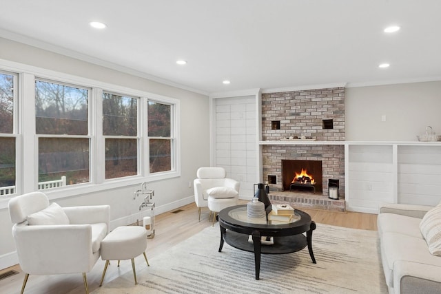 living room with a brick fireplace, crown molding, and light hardwood / wood-style flooring