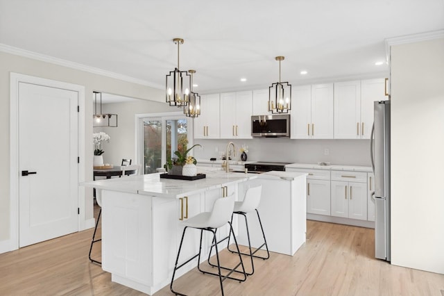 kitchen featuring appliances with stainless steel finishes, a kitchen island with sink, light hardwood / wood-style flooring, white cabinets, and hanging light fixtures