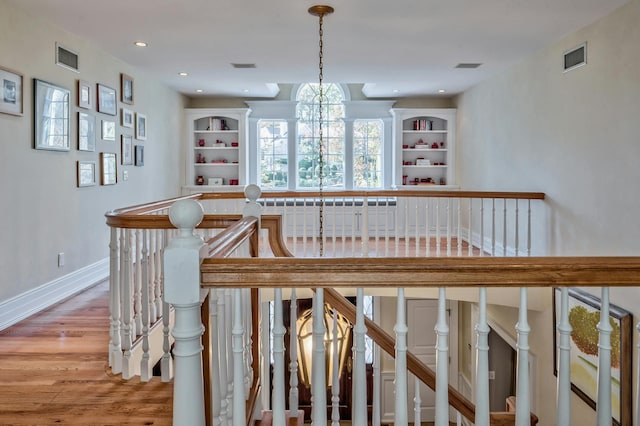 stairs with hardwood / wood-style floors, built in shelves, and a notable chandelier