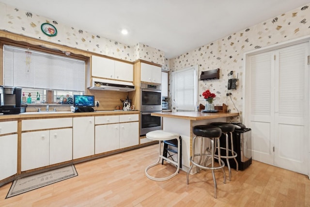 kitchen featuring white cabinetry, stainless steel double oven, a kitchen breakfast bar, light hardwood / wood-style flooring, and kitchen peninsula