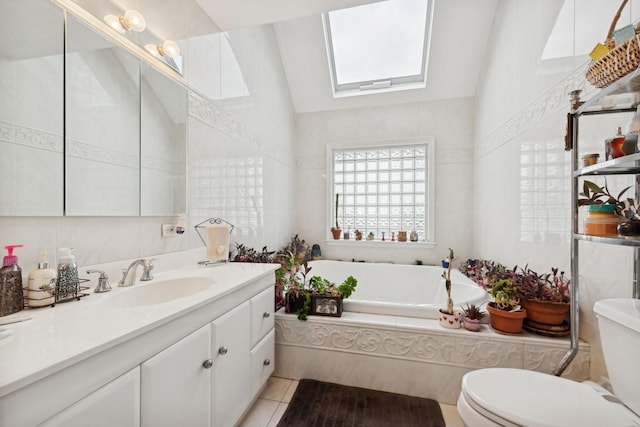 bathroom featuring tile patterned flooring, tiled tub, toilet, vaulted ceiling with skylight, and vanity