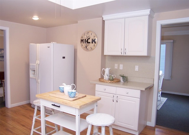 kitchen with tasteful backsplash, white cabinetry, white fridge with ice dispenser, and light hardwood / wood-style flooring