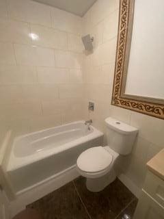 full bathroom featuring tiled shower / bath combo, toilet, tile walls, and vanity