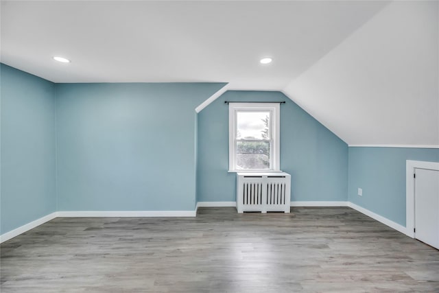 additional living space with radiator heating unit, light wood-type flooring, and vaulted ceiling