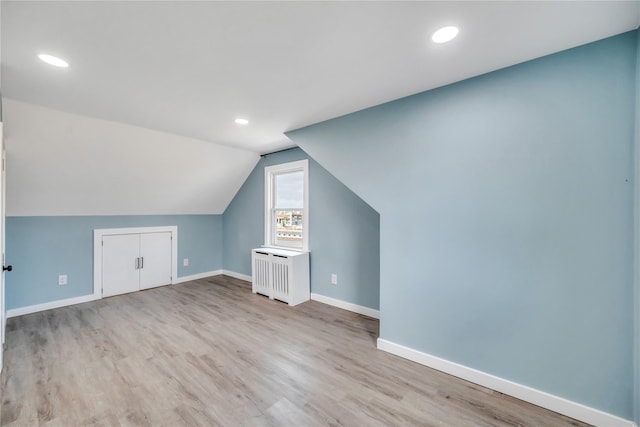 additional living space featuring radiator heating unit, light hardwood / wood-style flooring, and lofted ceiling