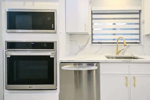 kitchen featuring white cabinets, appliances with stainless steel finishes, light stone countertops, and sink