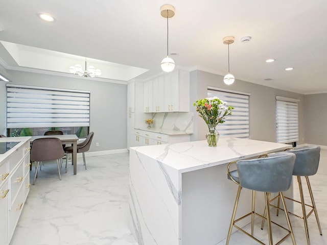 kitchen featuring white cabinetry, hanging light fixtures, a kitchen island, and light stone counters