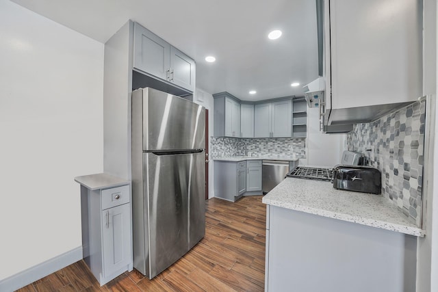 kitchen with backsplash, gray cabinets, appliances with stainless steel finishes, dark hardwood / wood-style flooring, and light stone counters