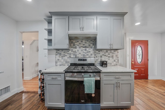 kitchen featuring hardwood / wood-style floors, stainless steel gas range oven, gray cabinets, tasteful backsplash, and light stone counters