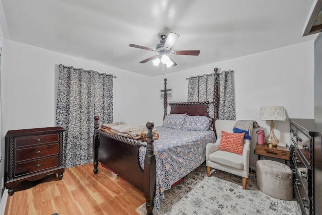 bedroom featuring a wall mounted AC, light hardwood / wood-style floors, and ceiling fan