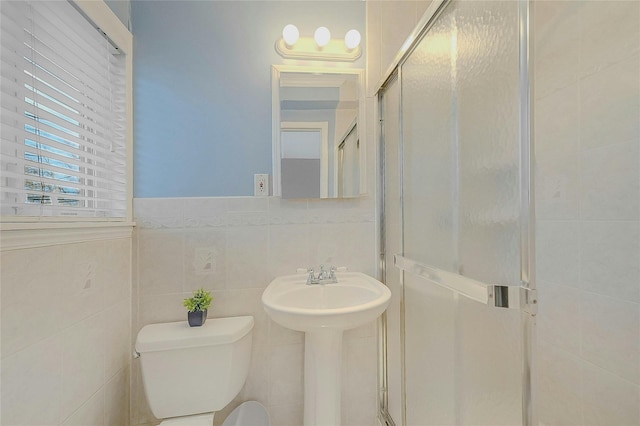 bathroom featuring toilet, tile walls, and a shower with shower door