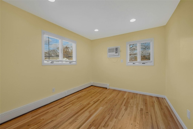 spare room with light wood-type flooring, an AC wall unit, and a baseboard heating unit