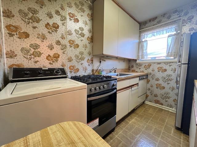 kitchen featuring sink, stainless steel appliances, light tile patterned floors, washer / clothes dryer, and white cabinets