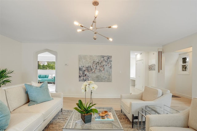 living area featuring a notable chandelier, baseboards, ornamental molding, light wood finished floors, and arched walkways