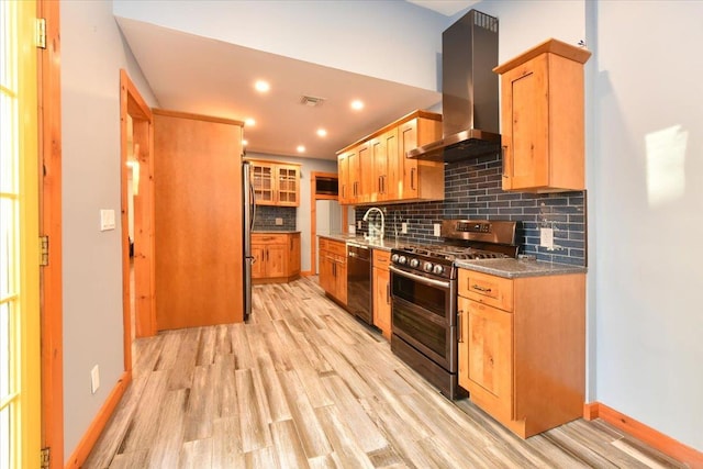 kitchen featuring decorative backsplash, appliances with stainless steel finishes, light wood-type flooring, wall chimney exhaust hood, and dark stone countertops