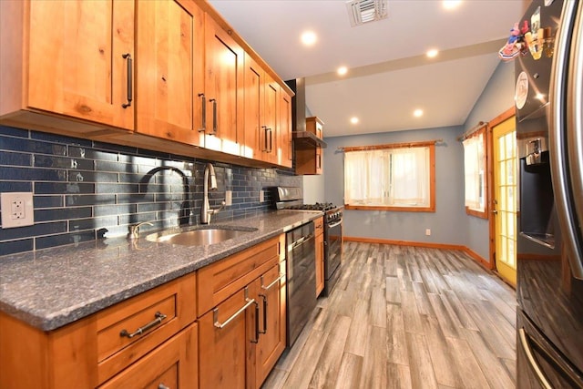 kitchen with dark stone counters, sink, stainless steel appliances, and light wood-type flooring