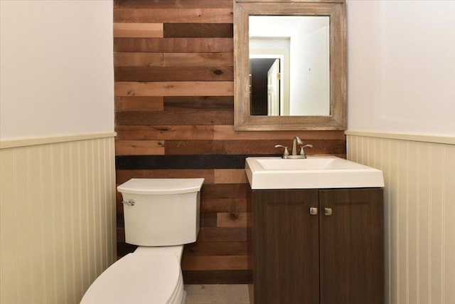 bathroom featuring vanity, toilet, and wooden walls