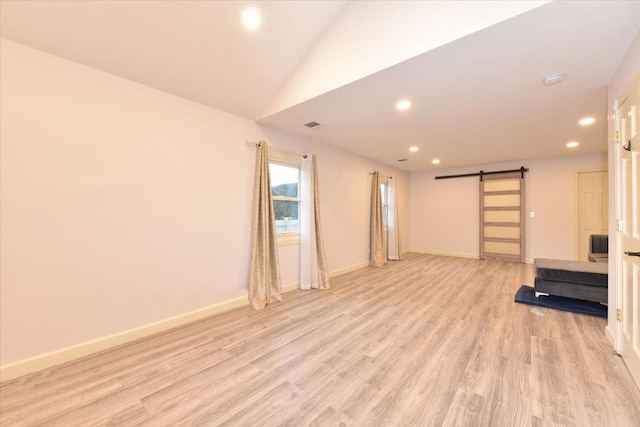 unfurnished living room featuring a barn door, light hardwood / wood-style floors, and lofted ceiling