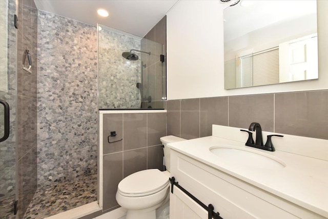 bathroom with a shower with door, vanity, tile walls, and toilet