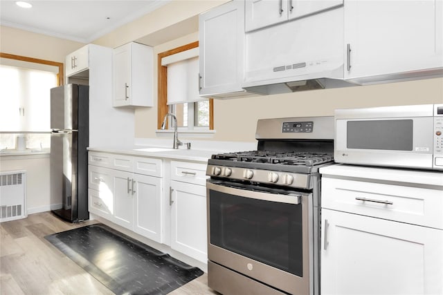 kitchen featuring white cabinetry, radiator heating unit, crown molding, appliances with stainless steel finishes, and light wood-type flooring