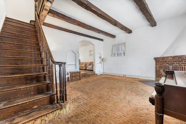 carpeted living room with stairway, arched walkways, and beamed ceiling