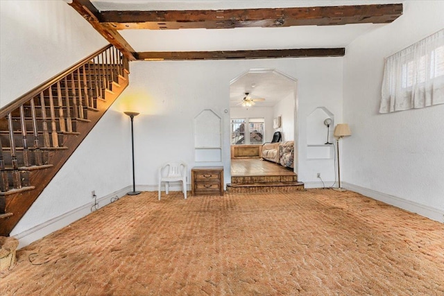 unfurnished living room featuring stairs, a ceiling fan, beam ceiling, and baseboards