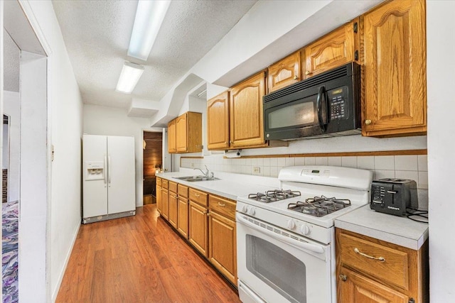 kitchen featuring white appliances, decorative backsplash, wood finished floors, light countertops, and a sink