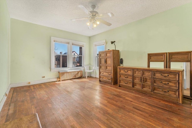 unfurnished bedroom featuring a textured ceiling, dark wood-style flooring, a ceiling fan, baseboards, and radiator heating unit