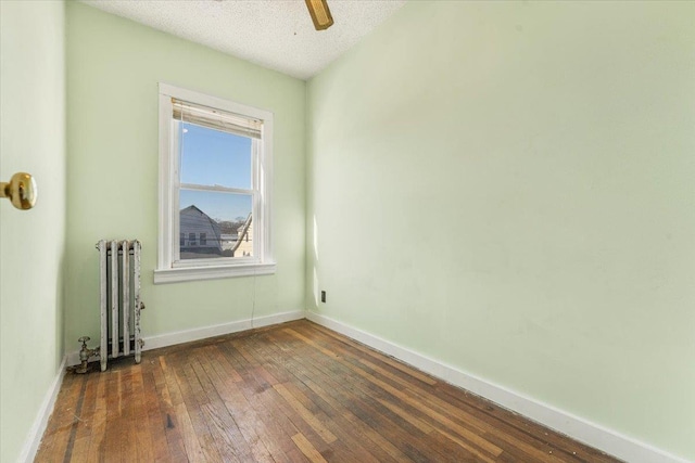 spare room featuring baseboards, radiator heating unit, ceiling fan, dark wood-type flooring, and a textured ceiling