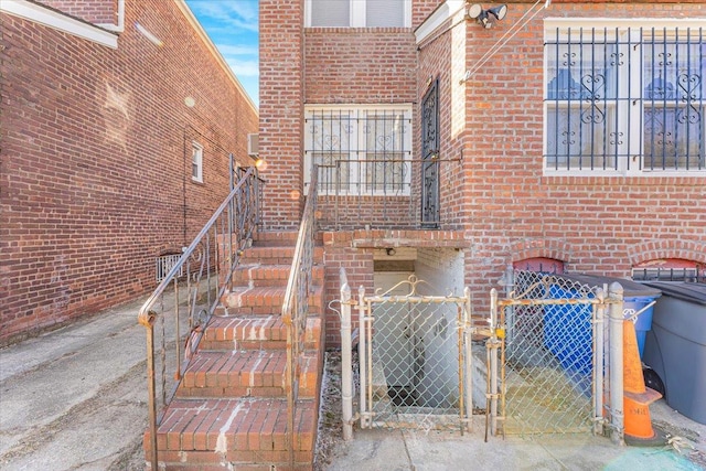 doorway to property with brick siding, central AC unit, fence, and a gate