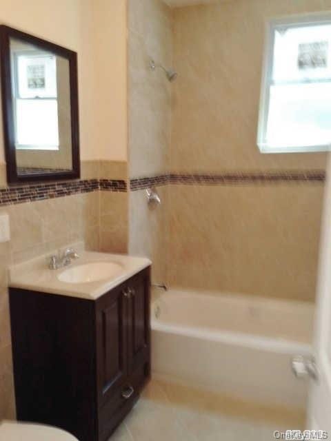 full bathroom featuring tile walls, vanity, tiled shower / bath combo, and toilet