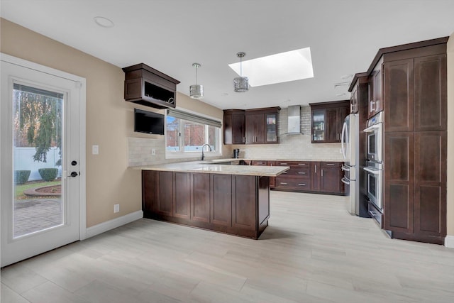 kitchen with wall chimney exhaust hood, dark brown cabinetry, kitchen peninsula, and stainless steel appliances