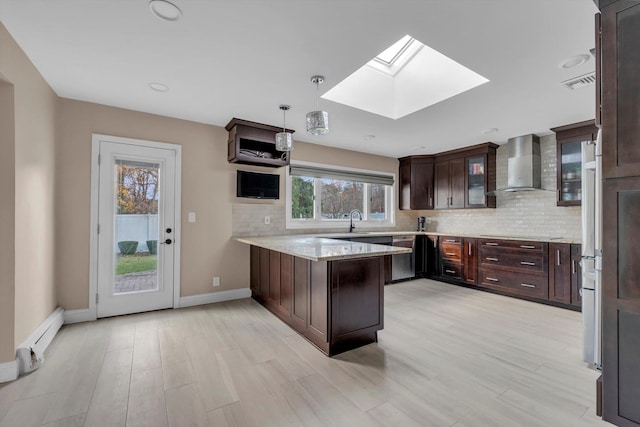 kitchen featuring kitchen peninsula, a skylight, a healthy amount of sunlight, and wall chimney range hood